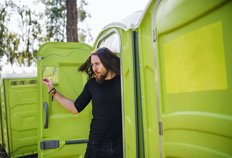 man coming out of a portable toilet at an event